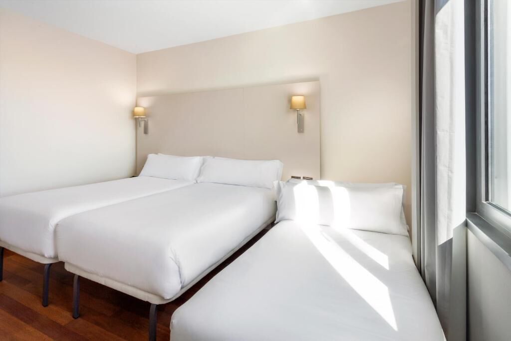 A hotel room with two beds, a wooden floor, and a window with curtains.