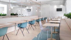 A modern dining area with long tables and chairs, a large mirror, and a flat-screen TV on the wall.