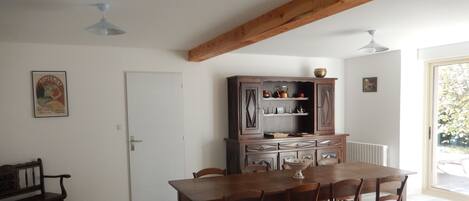 Un comedor con una mesa y sillas de madera, un mueble con utensilios de cocina, un banco y una puerta.