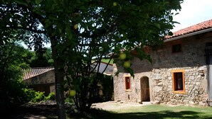 Un bâtiment en pierre doté de deux fenêtres et d’une porte, entouré de verdure.