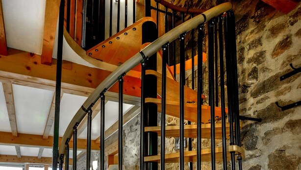 Un escalier en colimaçon avec des marches en bois et des rampes en métal, menant au deuxième étage.