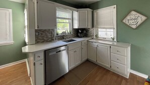 A kitchen with white cabinets, a dishwasher, a coffee maker, and a window with blinds. - Blue Door Cottage on Webster (Hastings)