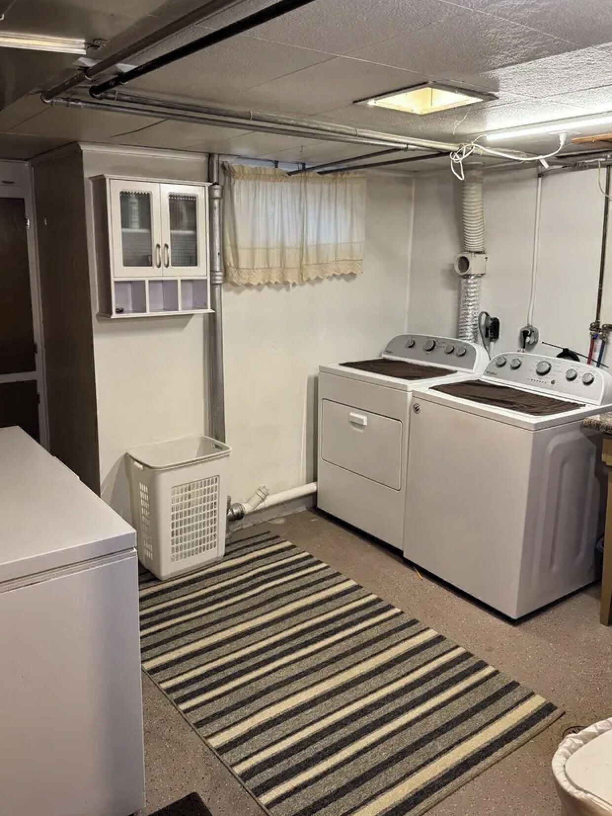 Pequeña lavandería con lavadora, secadora y un mueble pequeño.