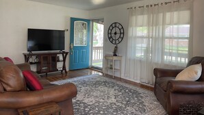 A living room with a blue door, a large clock, a TV, and two leather sofas. - Blue Door Cottage on Webster (Hastings)