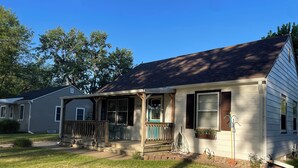 A single-story house with a porch, a visible number '110' on the door, and a small garden area with a hose. - Blue Door Cottage on Webster (Hastings)