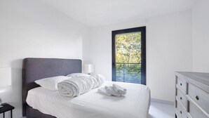Une chambre à coucher comprenant un lit, une commode, une table de chevet et une fenêtre donnant sur des arbres.