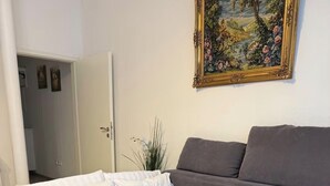 Ein Schlafzimmer mit einem Bett, einem grauen Sofa, einem Bild an der Wand und einer Tür zu einem anderen Raum.