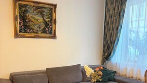 Ein modernes Wohnzimmer mit einem grauen Ecksofa, einem runden Couchtisch aus Holz und einem gerahmten Landschaftsbild an der Wand.