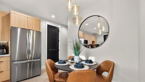 A modern kitchen with stainless steel appliances, a dining area with leather chairs, and a large mirror on the wall. - Welcome to The Desert Rose Guesthouse – Where Desert Skies Meet Rooftop Vibes (Hurricane)