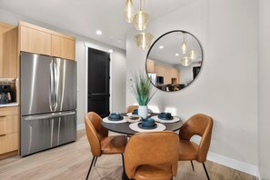 Une cuisine moderne équipée d’appareils électroménagers en acier inoxydable, un coin repas avec des chaises en cuir et un grand miroir au mur.