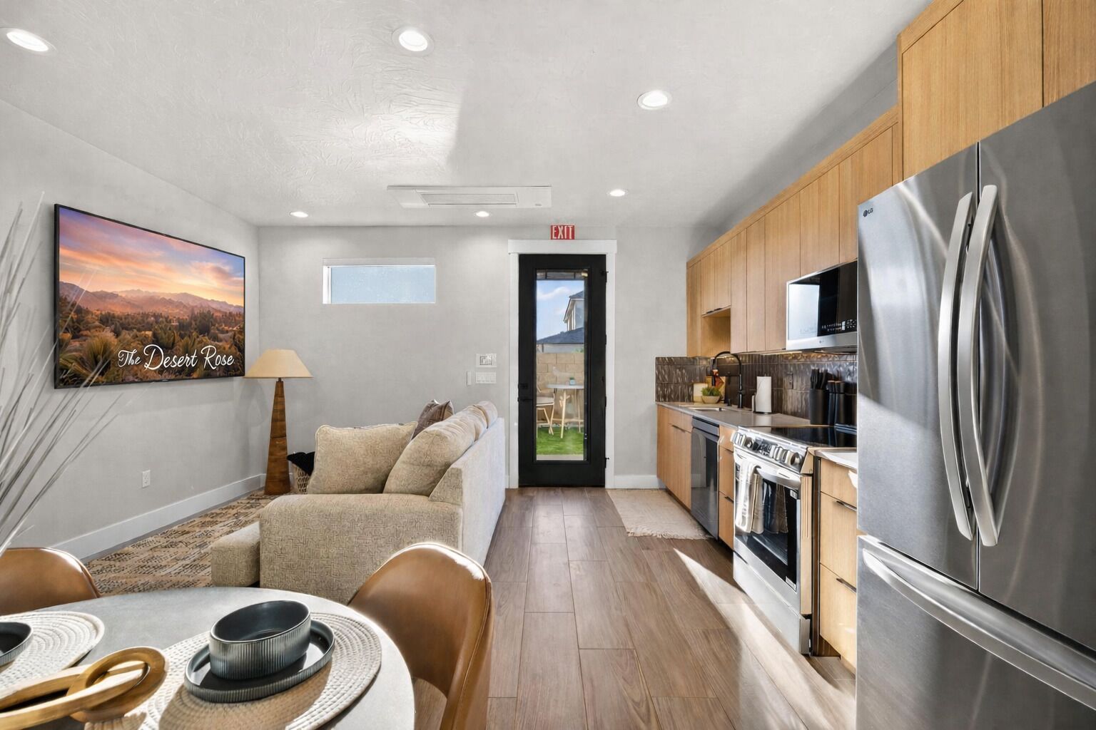 A modern kitchen with stainless steel appliances, a dining area with a table and chairs, and a living room with a sofa and a painting.