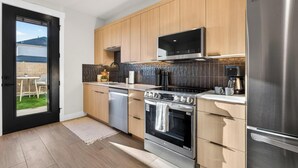 A modern kitchen with wooden cabinets, stainless steel appliances, and a view to the outside. - Welcome to The Desert Rose Guesthouse – Where Desert Skies Meet Rooftop Vibes (Hurricane)