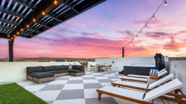 A rooftop patio with a checkered floor, outdoor seating, string lights, and a view of the landscape. - Welcome to The Desert Rose Guesthouse – Where Desert Skies Meet Rooftop Vibes (Hurricane)