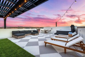 A rooftop patio with a checkered floor, outdoor seating, string lights, and a view of the landscape. - Welcome to The Desert Rose Guesthouse – Where Desert Skies Meet Rooftop Vibes (Hurricane)