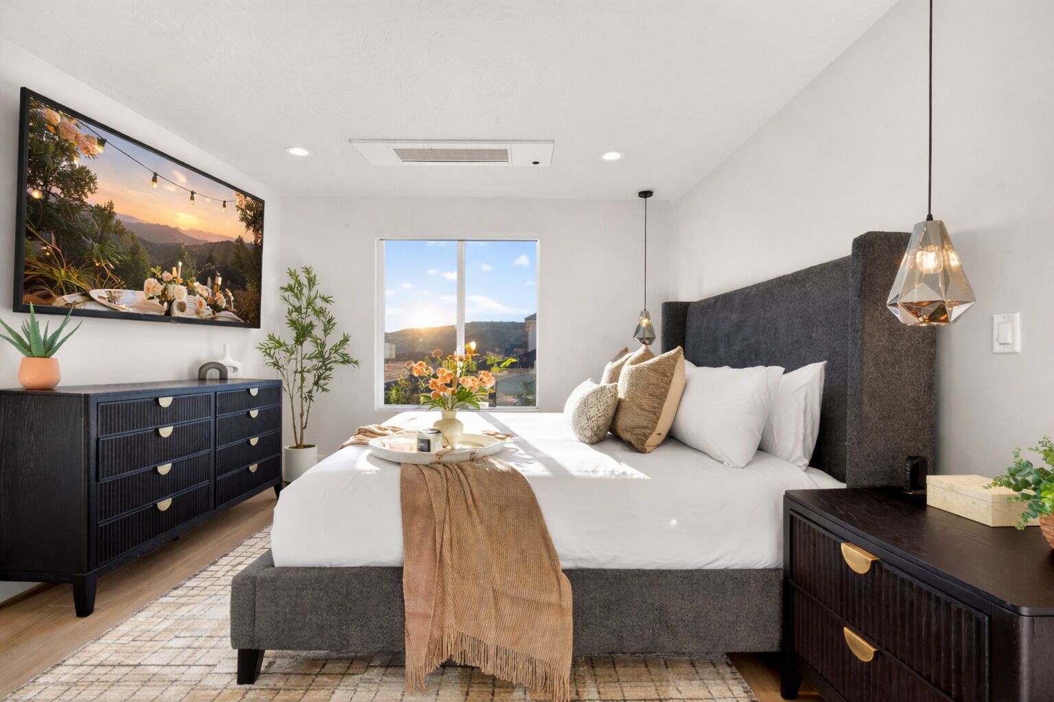 A modern bedroom with a large bed, a dresser, a nightstand, a painting, and a window with a view.