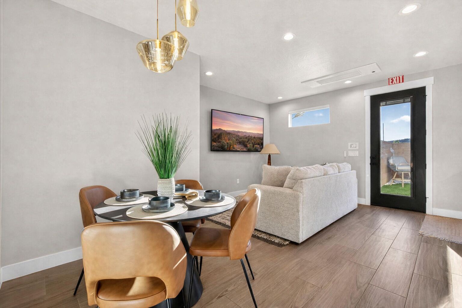 A modern living room with a dining area, a sofa, a coffee table, and a view of the outdoors through a door.