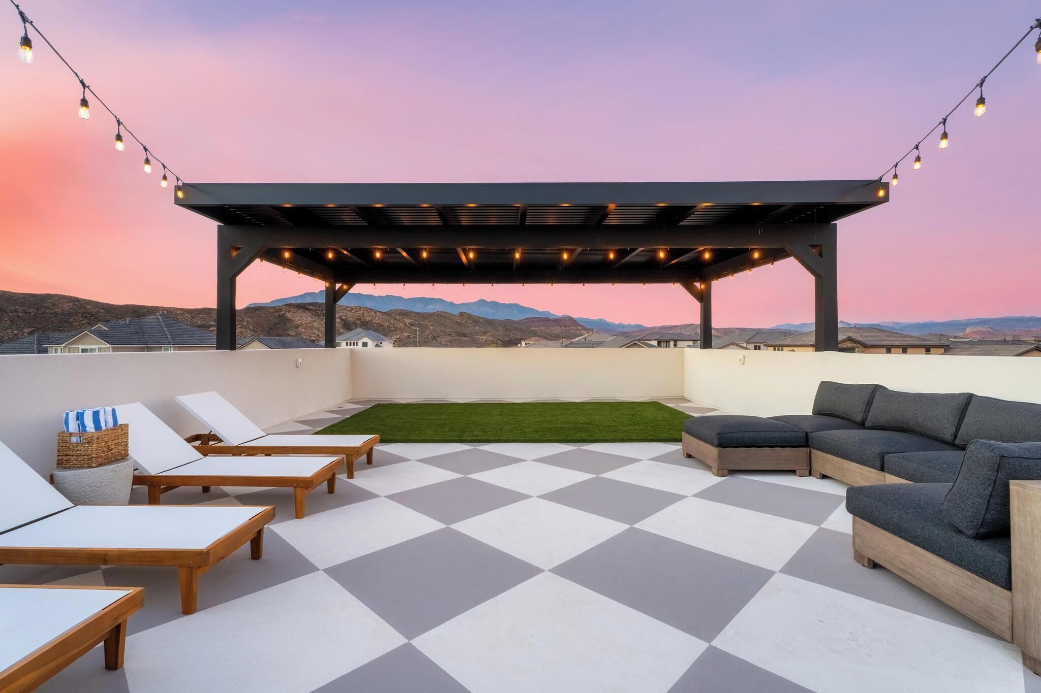A rooftop terrace with a checkered floor, lounge chairs, a sofa, and string lights.
