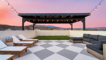 A rooftop terrace with a checkered floor, lounge chairs, a sofa, and string lights.