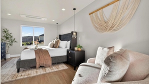 A bedroom with a bed, bedside table, nightstand, and a large window. - Welcome to The Desert Rose Guesthouse – Where Desert Skies Meet Rooftop Vibes (Hurricane)