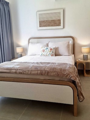 Una cama bien hecha con un cabecero marrón, dos lámparas de noche y una obra de arte enmarcada sobre la cama.