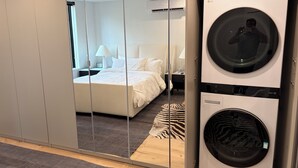 Una habitación de hotel con cama, espejo, lavadora y armario.