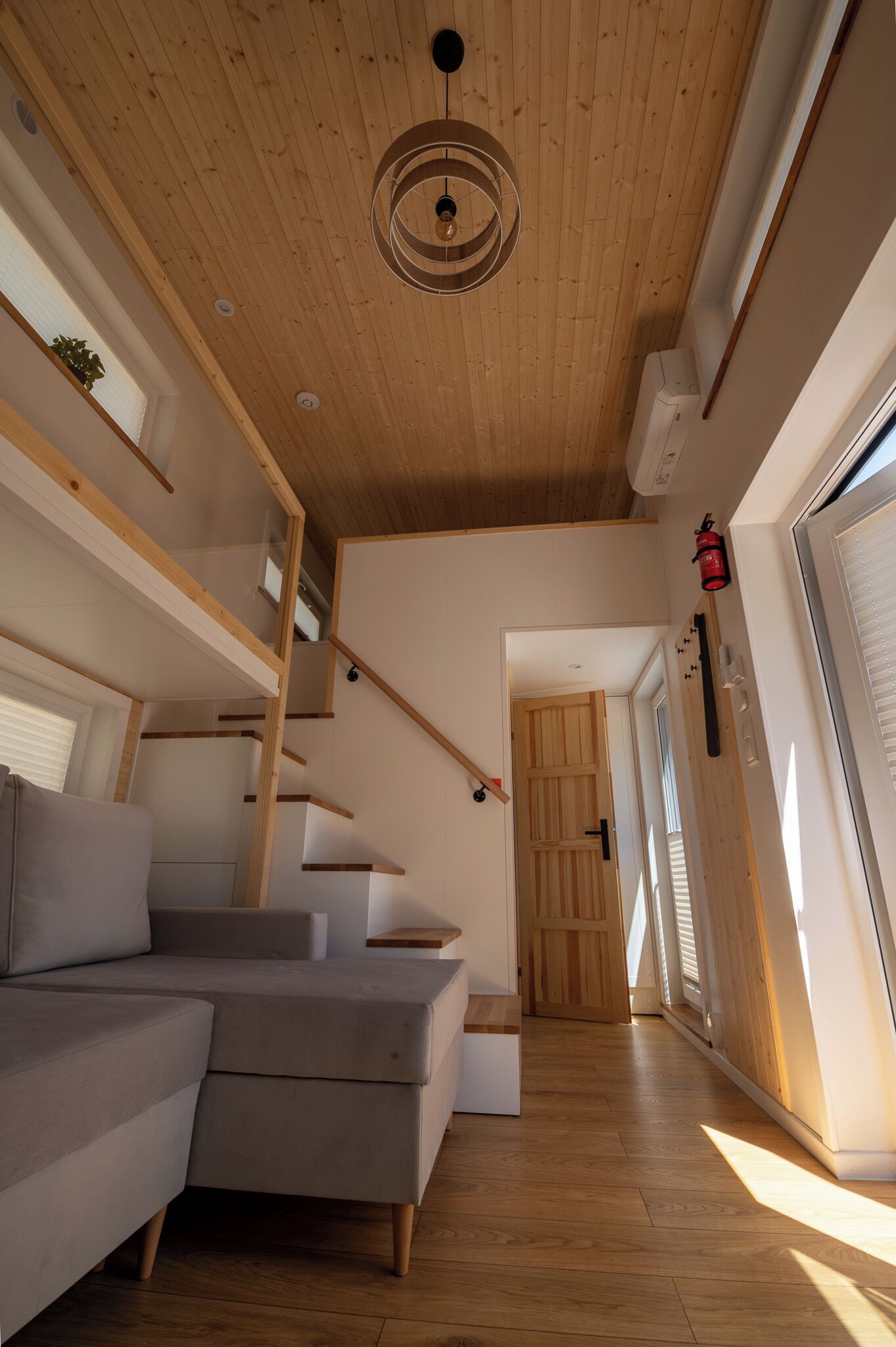 Ein modernes Interieur mit Holzboden, einer Treppe, einem grauen Sofa und einer Tür zu einem anderen Raum.