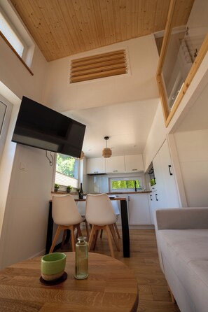 Una cocina compacta con comedor, un televisor montado en la pared y una ventana con persianas.