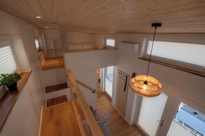 Un interior con varios niveles, pisos de madera, una escalera, una lámpara colgante y una vista por la ventana.
