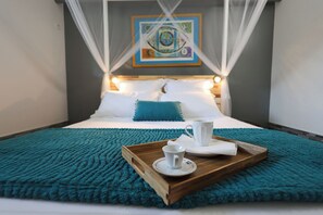 A neatly made bed with a blue throw blanket, a wooden tray with a white cup and saucer, and a painting above the bed. - Villa Écume Verte - 2 bedrooms, terraces, quiet & close to Sainte-Anne beaches (Sainte-Anne)
