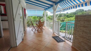 A covered balcony with a table and chairs, a doormat, and a view of greenery. - Villa Écume Verte - 2 bedrooms, terraces, quiet & close to Sainte-Anne beaches (Sainte-Anne)