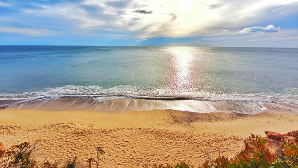 Ein Strand mit klarem Wasser, sandigem Ufer und einem teils bewölkten Himmel.