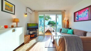 Ein modernes Wohnzimmer mit Flachbildfernseher, einer Couch, einem Essbereich mit Tisch und Stühlen sowie einem Balkon mit Aussicht.