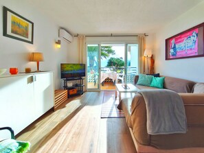 A modern living room with a flat-screen TV, a sofa, a dining area with a table and chairs, and a balcony with a view. - Beachfront apartment with swimming pool Miami Platja (Miami Platja)