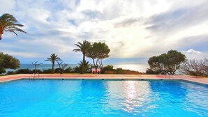Ein Swimmingpool mit Blick auf das Meer, umgeben von Palmen und einem wolkenlosen Himmel.