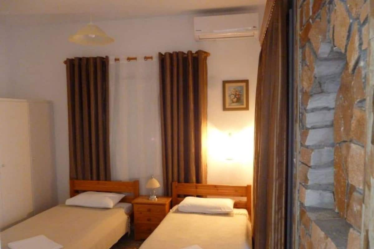 A hotel room with two beds, a nightstand, an air conditioning unit, and a stone wall.