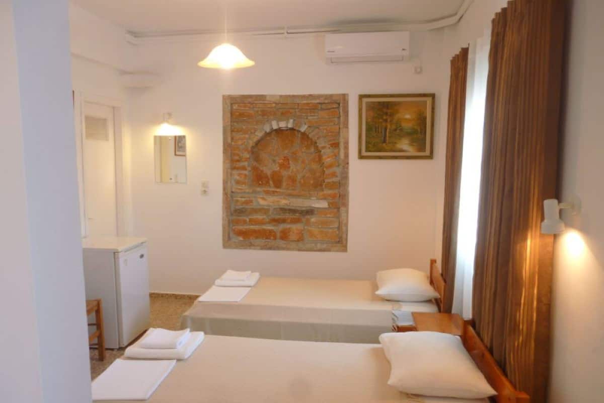 A room with two beds, a small desk, a mirror, a fireplace, and a painting.