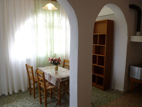 A dining area with a table, chairs, a vase with flowers, a bookshelf, and a stove. - Vasilis Ios Place II (Ios)
