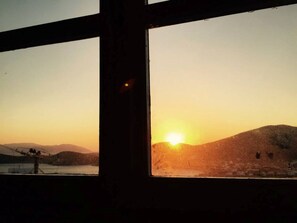 A window with a view of a sunset over a hilly landscape.