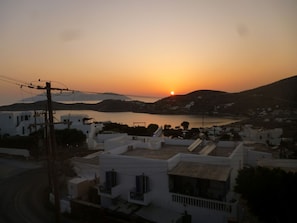 A coastal town at sunset with white buildings, a body of water, and a hilly landscape. - Vasilis Ios Place II (Ios)