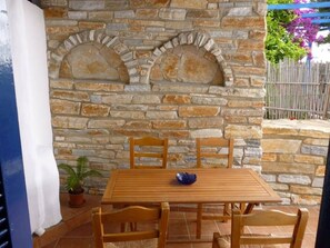 A stone wall with a wooden table and chairs, a potted plant, and a blue railing.