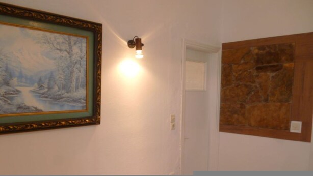 A room with a framed painting, a wall-mounted light fixture, and a stone accent wall.