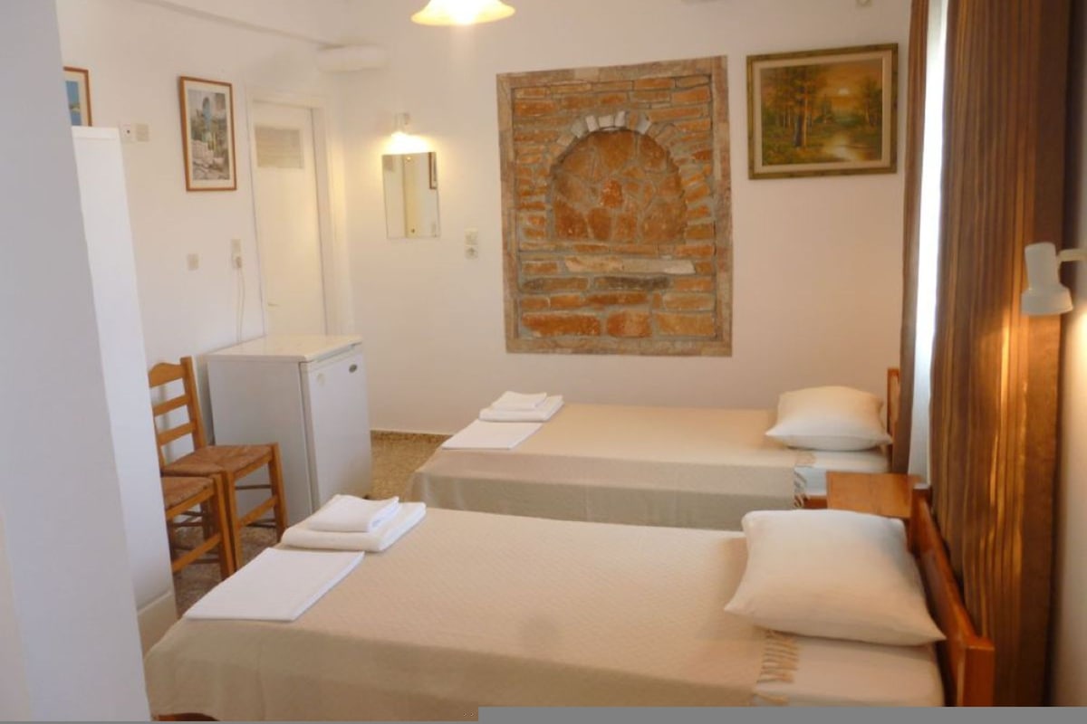 Habitación de hotel con dos camas, un escritorio pequeño, una silla, un espejo y un adorno de pared de ladrillo.