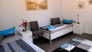 Une chambre à coucher comprenant un lit, une chaise, une table de chevet, une lampe, un tableau et une petite table sur laquelle est posé un vase de fleurs.