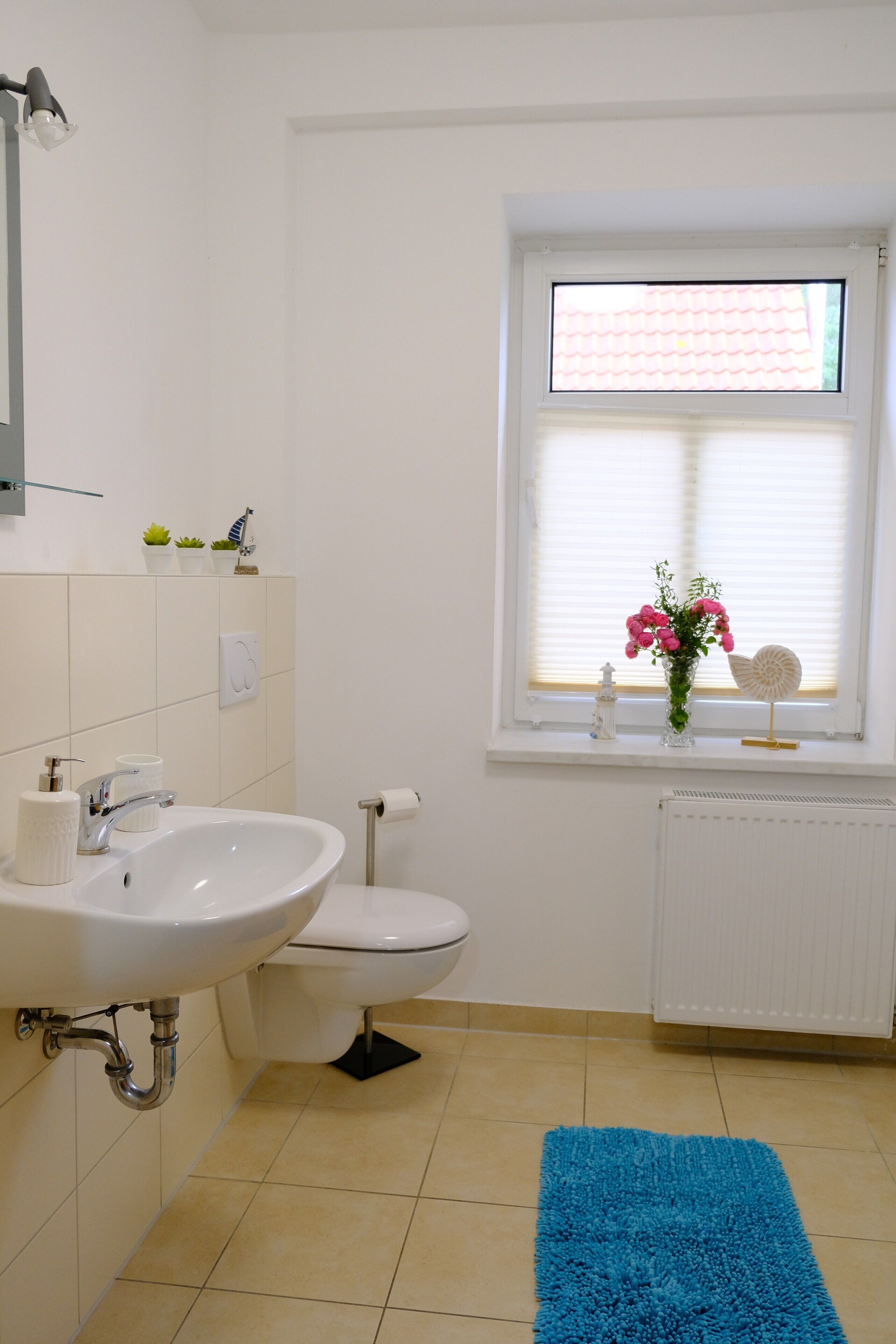 A bathroom with a white sink, toilet, and window with blinds.