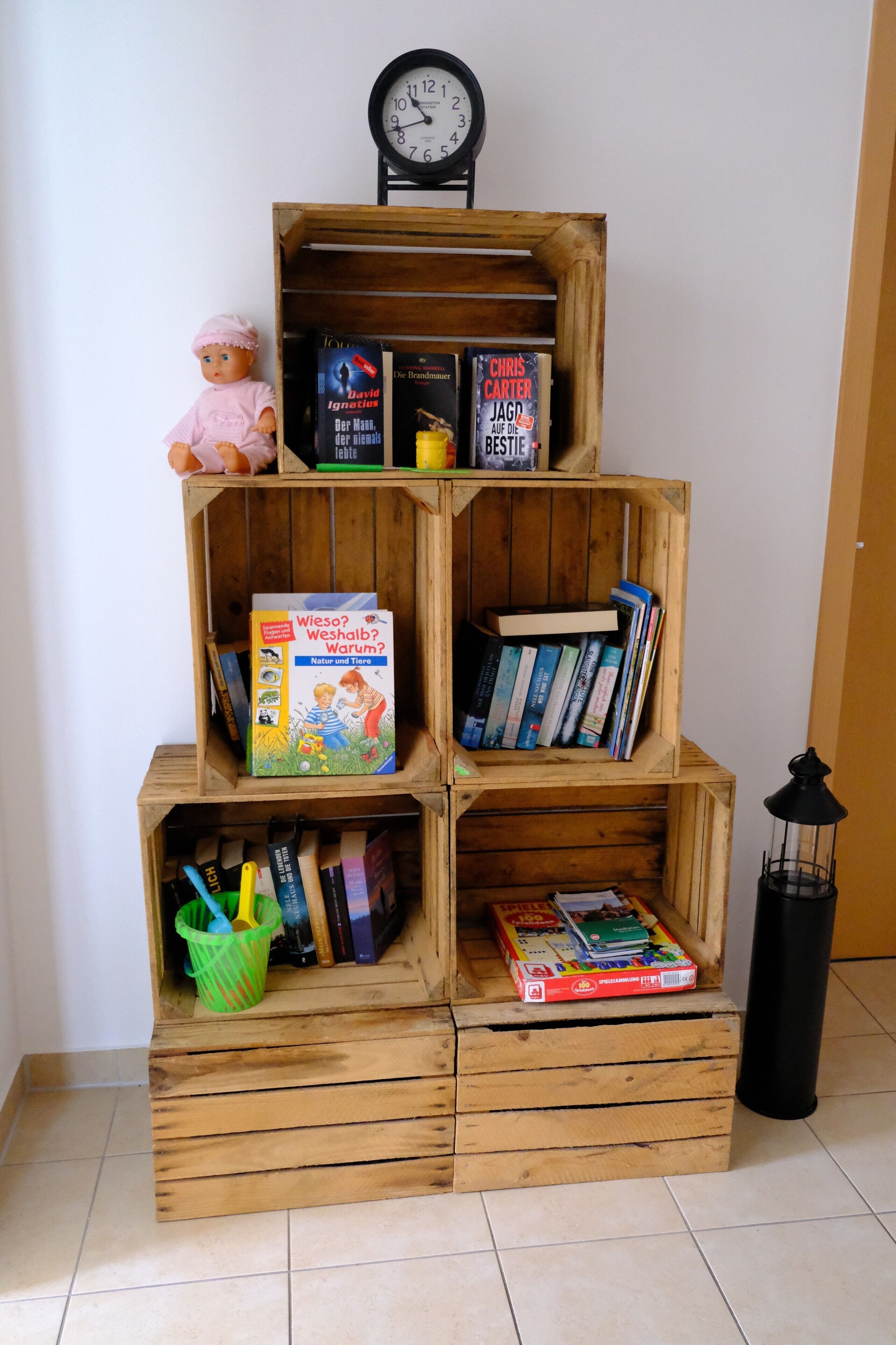 Ein Bücherregal aus Holz mit Büchern, einer Puppe, einer Uhr und einer Laterne.