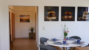 Un coin repas avec une table ronde, des chaises et un tableau représentant un hamburger, accroché au mur.