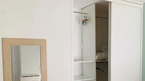 Un dormitorio con cama, armario con estantes y espejo.