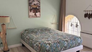 Un dormitorio con una cama, un ventilador de techo, una lámpara de pared, un cuadro y una ventana con cortinas.