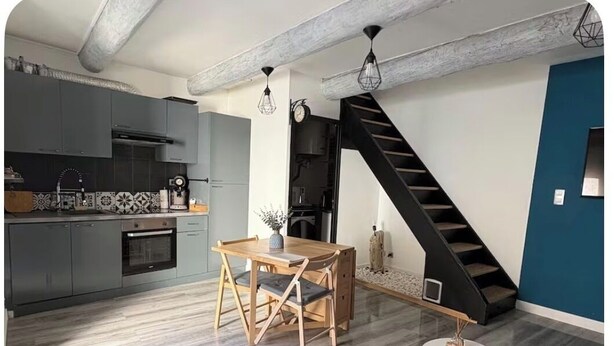 Una cocina moderna con armarios grises, una mesa de comedor de madera y una escalera negra.