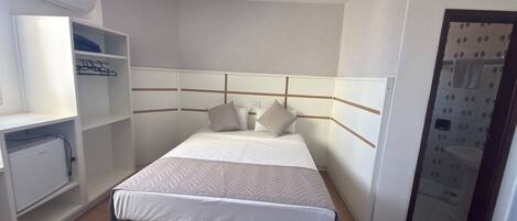 Habitación de hotel con cama, armario empotrado y escritorio pequeño.